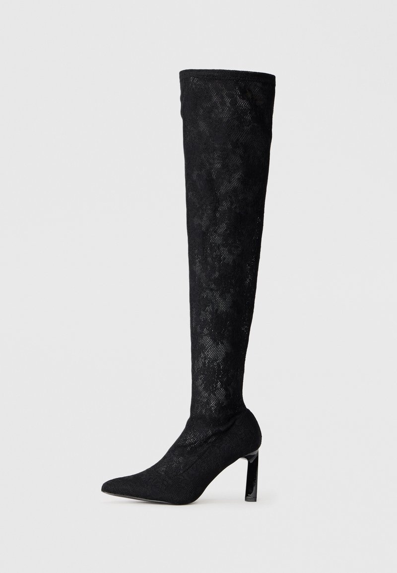 Botas negras de tacón alto por encima de la rodilla, hechas de tejido texturizado, con puntera afilada y un tacón brillante alto con un patrón parecido a encaje.