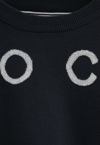 Tissu tricoté foncé avec des lettres majuscules blanches O et C près d'un col côtelé.