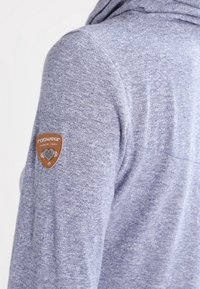 Grauer Struktur-Hoodie mit entspannter Passform, ausgestattet mit einem braunen Leder-Logopatch auf der linken Schulter und einer Kapuze.