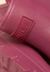 Růžové gumové sandály s texturovanými pásky a podrážkou, na nichž je vystouplá logo značka. Design zahrnuje odolný materiál a jednoduchý, moderní tvar.