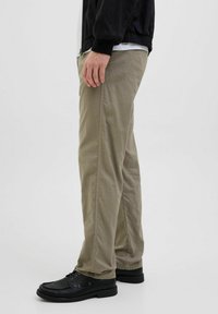 Beige cotton pants with a straight cut, featuring side seams, and worn with black shoes. Smooth texture and durable design.