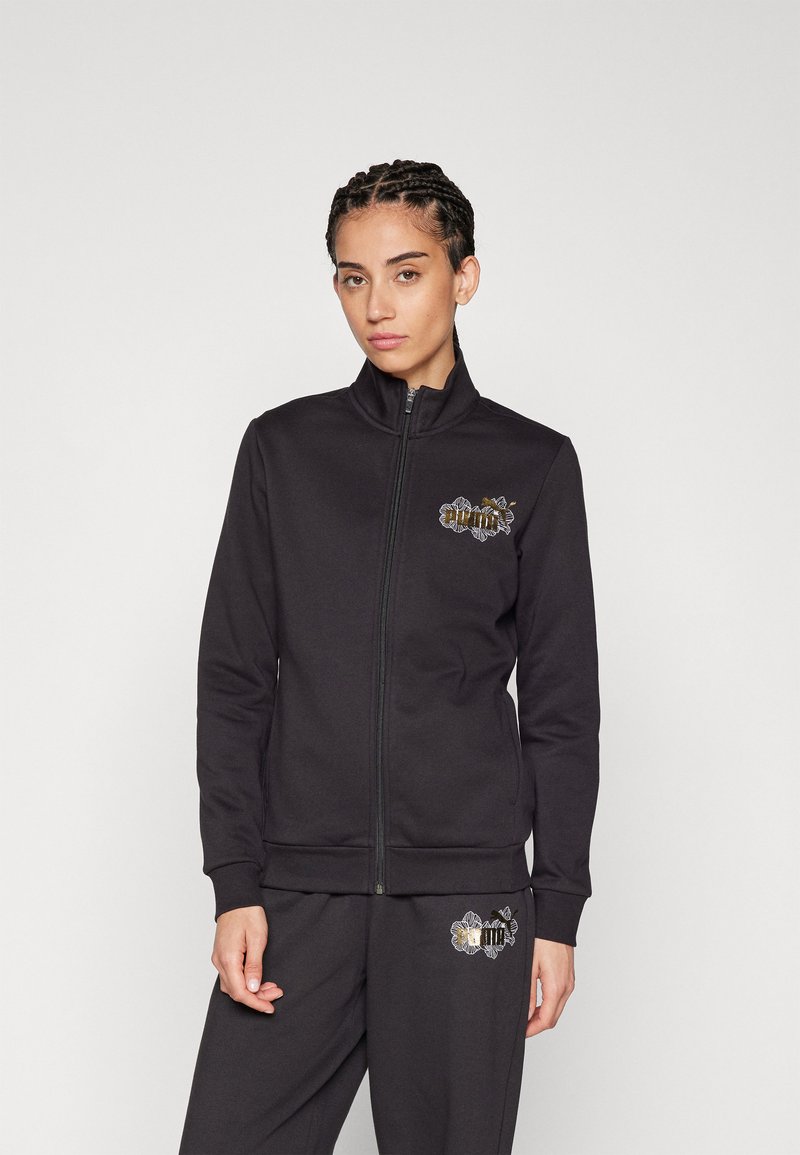 Giacca nera con zip realizzata in un tessuto morbido, dotata di una zip frontale, colletto alto e un design ricamato decorativo sul petto e sulla cintura.