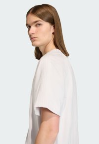 Bijela kratka majica s okruglim izrezom, ukrašena teksturiranim detaljima na ramenima. Glatka, lagana tkanina.