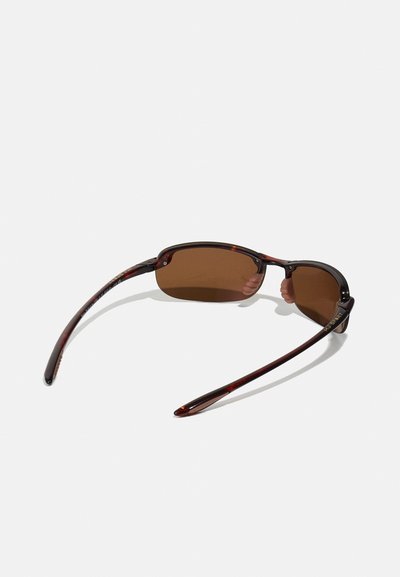 Des lunettes de soleil teintées marron avec une monture en écaille de tortue. Le design présente des branches fines et une forme légère et courbée pour le confort.