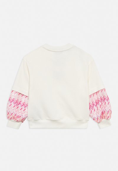 Άσπρη μπλούζα με μακριά, φουσκωτά ροζ μανίκια με ζιγκ-ζαγκ μοτίβο σε διάφορες αποχρώσεις του ροζ και του κόκκινου.