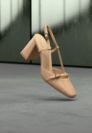 Chaussure à talon bloc couleur chair avec bout pointu, brides réglables à la cheville et détail de boucle plate. Texture en cuir lisse.
