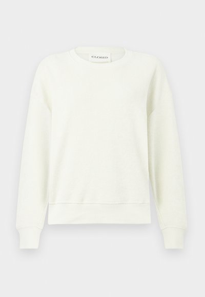 Ανοιχτό μπεζ φούτερ με στρογγυλή λαιμόκοψη, μακριά μανίκια, ριμπ μανσέτες και τελείωμα, και απαλό, υφασμάτινο ύφασμα με υφή. Η ετικέτα δείχνει "CLOSED."