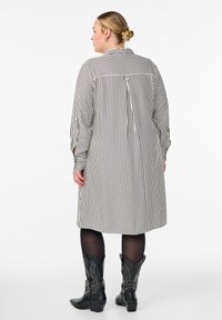 Czarna i biała w paski sukienka koszulowa z kołnierzykiem, zapięciem na guziki z tyłu i długimi rękawami; zestawiona z czarnymi kowbojkami z dżetami.