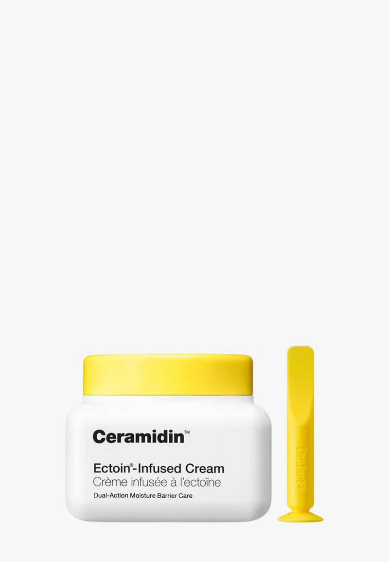 Crème Ceramidin infusée d'Ectoin dans un récipient rond blanc avec un couvercle jaune, accompagnée d'un applicateur jaune assorti.