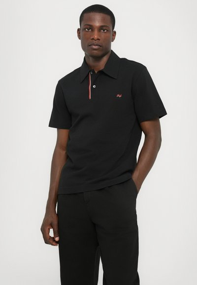 Polo noir en coton, avec des manches courtes, une patte de boutonnage et un détail rayé rouge et blanc sur le col.