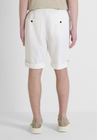 Bermuda bianche con vestibilità rilassata, orli risvoltati, due tasche posteriori e dettagli dei bottoni neri, realizzate in tessuto leggero.