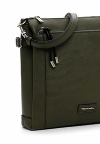 Borsa a tracolla in pelle verde con texture liscia, manico superiore, accessori in argento e patch con logo. La borsa presenta una chiusura con zip e dettagli neri.