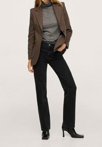 Blazer de cuadros marrones sobre un suéter de cuello alto gris, combinado con jeans rectos de tiro alto negros y botas de tacón negras hasta el tobillo.