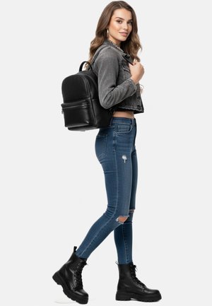 Zwarte leren rugzak met afgeronde vorm, verstelbare bandjes, voorvak, gedragen over een grijze denim jas, gecombineerd met blauwe versleten skinny jeans en zwarte combatlaarzen.