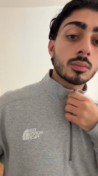 Chaqueta gris con cremallera y cuello alto, con un logo en el pecho izquierdo. Textura suave, tejido ligero y diseño minimalista.