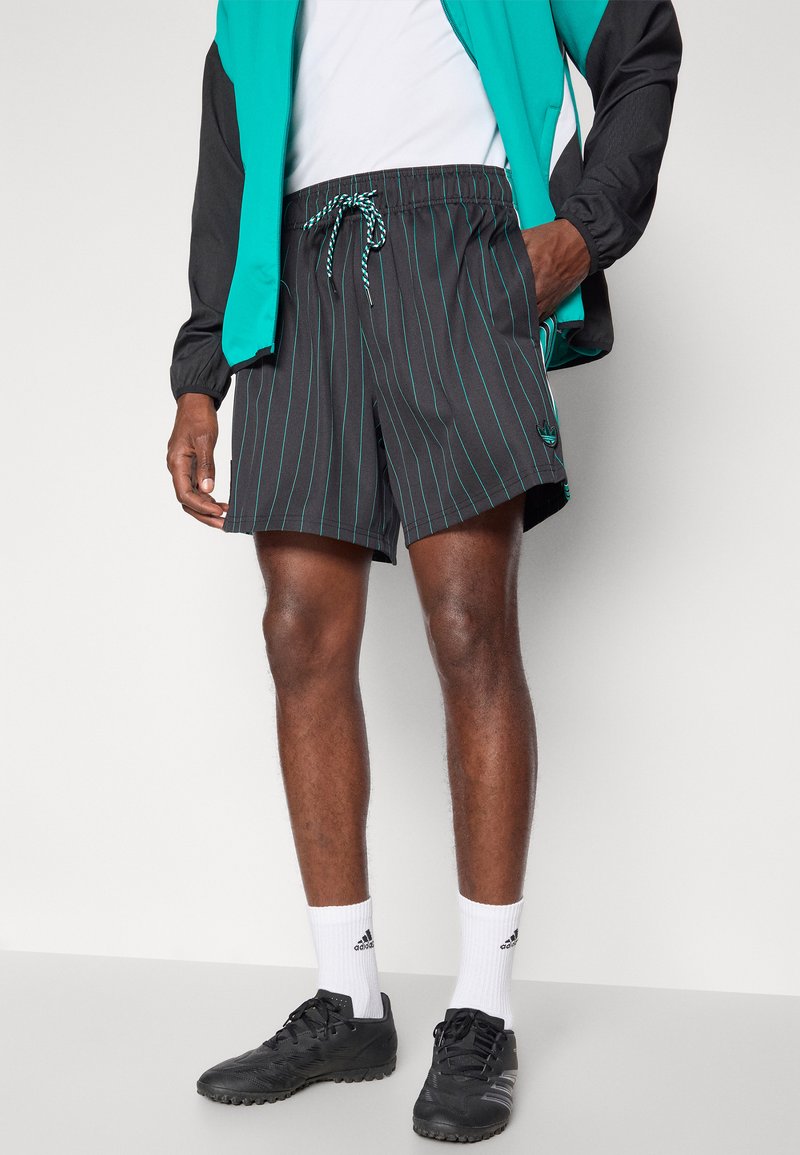 Shorts noirs avec des rayures turquoise, taille élastique et cordon de serrage ; associés à des chaussures de sport noires et des chaussettes blanches.