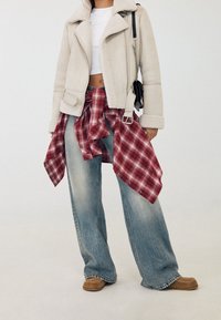 Béžová kožešinová bunda, bílý crop top, červená kostkovaná košile uvázaná v pase, světlé modré široké džíny a hnědé slip-on boty.