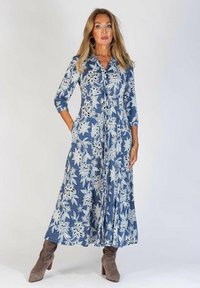 Lång denimklänning med vitt blommönster, skjortkrage, trekvarts ärmar, sidofickor och flödande kjol. Bärs med bruna klackstövlar.