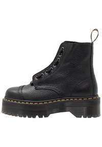 Botte de cheville en cuir noir avec finition texturée, bout arrondi, six œillets en métal, couture jaune et semelle en caoutchouc translucide et épaisse.