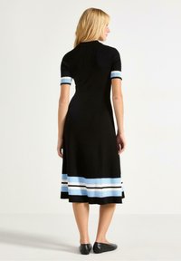 Musta mekko, jossa on ribbed rakenne, lyhyet hihat, joissa on vaaleansiniset yksityiskohdat, ja hame, jossa on vaaleansinisia ja mustia vaakaraitoja.