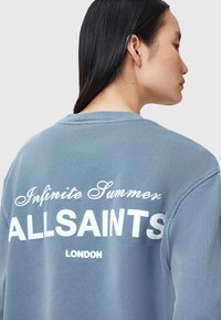 Modrá bavlněná mikina s kulatým výstřihem a bílým nápisem „Infinite Summer ALLSAINTS LONDON“ na zádech. Hladká textura.
