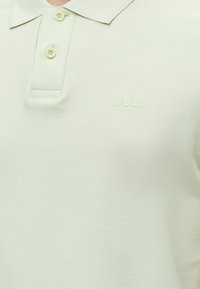Polo vert clair avec deux boutons et logo « BOSS » brodé sur la poitrine gauche.