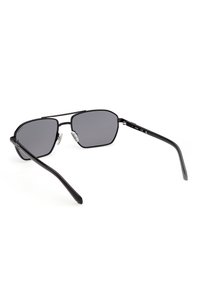 Gafas de sol con montura negra de metal, lentes rectangulares oscuras y almohadillas nasales ajustables, vistas desde atrás sobre un fondo blanco.