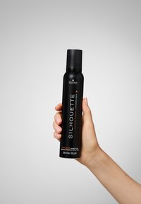 Flacon mousse cylindrique noir avec un bouchon noir. Le texte comprend "SILHOUETTE", "super hold" et "200 ml". Main tenant le flacon.