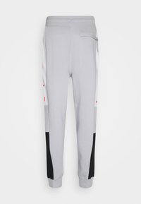 Pantalon de jogging gris clair avec des panneaux noirs sur le bas des jambes, des bandes blanches sur les côtés et une petite poche à rabat sur la hanche droite.