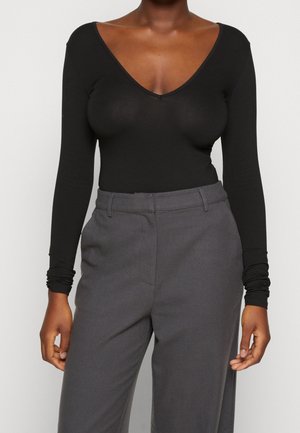 Musta pitkähihainen body, jossa syvä V-pääntie, istuva malli ja sileä pinta, yhdistetty korkeavyötäröisiin harmaisiin housuihin.