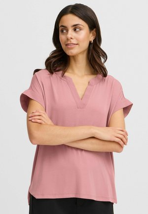 Blouse rose à manches courtes avec un col en V et des poignets retroussés, faite en tissu lisse, présentant une coupe décontractée et des fentes latérales à l'ourlet.