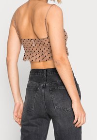 Top corto a pois marroni con orlo a frangia, spalline sottili regolabili, abbinato a jeans neri a vita alta con tasche posteriori.