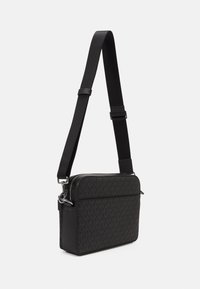 Zwarte crossbody tas met een gestructureerd ontwerp dat een monogram patroon heeft. Het heeft een ritssluiting en een verstelbare schouderband voor gemak.