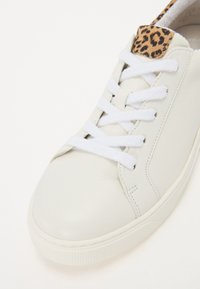 Sneaker in pelle bianca con punta arrotondata, lacci piatti bianchi e un accento in stampa leopardata sul tallone. Texture liscia e design minimalista.