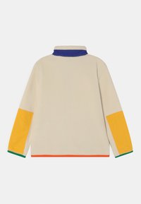 Kremowy polarowy sweter z niebieskim kołnierzem, pomarańczowym wykończeniem i żółtymi akcentami na rękawach. Miękka tekstura i luźny krój, z bocznymi kieszeniami.
