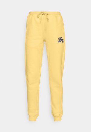 Gule joggebukser laget av mykt bomullsmateriale, med elastisk midjebånd og justerbar snøring, samt en liten blå logo på venstre lår.