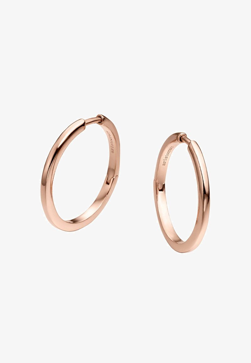 Pendientes de aro en oro rosado con un acabado suave y pulido, que presentan un diseño sin costuras y un cierre seguro. Tienen forma circular y tamaño mediano.