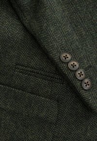 Manche de veste en laine vert foncé à chevrons, avec quatre boutons foncés et une poche fendue.