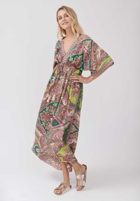 Robe maxi fluide et à motifs en vert, rose et beige, avec un décolleté en V et une taille élastique. Associée à des sandales à glissière métalliques.