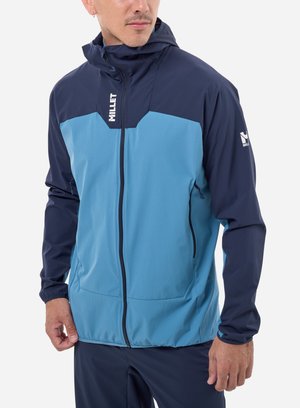 Homme portant une veste Millet bicolore bleu avec une fermeture éclair frontale et des logos de la marque visibles sur la poitrine et la manche.