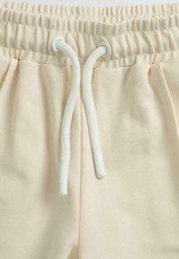 Ceinture élastique beige avec cordon de serrage blanc sur tissu doux, montrant les détails de la couture et le matériau froncé.