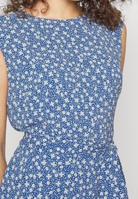 Blå blommig klänning med vita mönster, korta ärmar, rund halsringning och rynkad midja. Lättviktig tyg med en något texturerad yta.