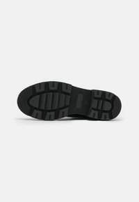 Sole di scarpa in gomma nera con superficie testurizzata, scanalature profonde, forma arrotondata e tacco piatto per una migliore trazione.