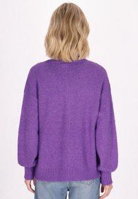 Suéter oversized morado con una textura suave, hombros caídos, dobladillo acanalado y mangas largas, combinado con jeans de color azul claro.