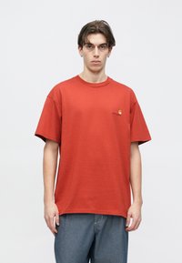 Κόκκινο βαμβακερό μπλουζάκι με κοντά μανίκια και στρογγυλή λαιμόκοψη. Διαθέτει μικρό κίτρινο λογότυπο στο αριστερό στήθος. Χαλαρή εφαρμογή, λεία υφή.