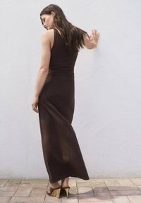 Rochie maxi de culoare maro, adaptată pe corp, cu un design fără mâneci, dintr-un material texturat și cu o fustă fluidă. Prezintă detalii pliate la spate și o finisare netedă.