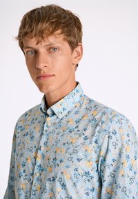 Ljusblå blommig skjorta med knapp-down krage. Har små mönster av gula och blå blommor, tillverkad av bomull och med en avslappnad passform.