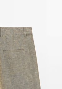 Pantalon en lin beige montrant la partie supérieure avec ceinture, passants de ceinture et une poche arrière passepoilée unique sur fond blanc.