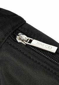 Czarna torba z tkaniny o gładkiej fakturze, z metalowym suwakiem z nazwą marki. Zamek błyskawiczny jest obramowany kontrastującym czarnym materiałem.