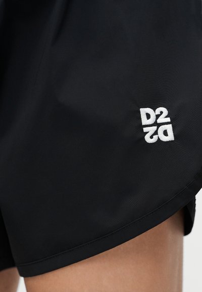 Μαύρα σορτς με λευκό κεντημένο λογότυπο "D2" κοντά στο τελείωμα του μηρού, εμφανίζοντας μέρος του ποδιού ενός ατόμου.
